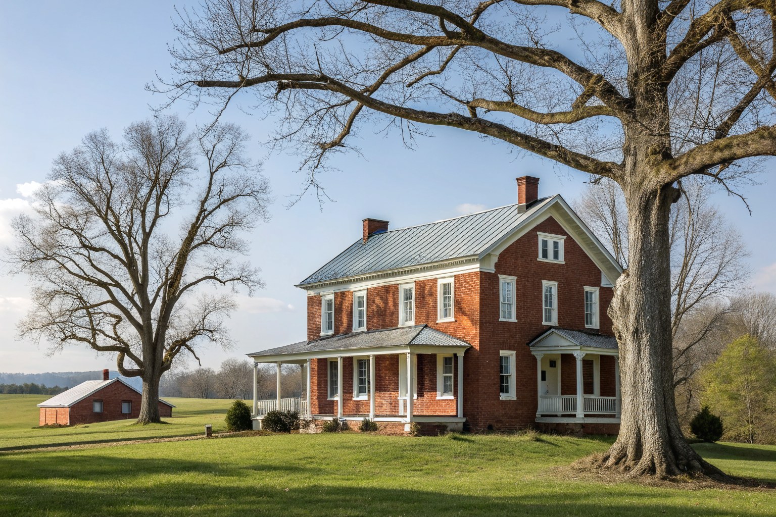 A restored early 1800s red brick farmhouse with a standing-seam metal roof under old oaks
