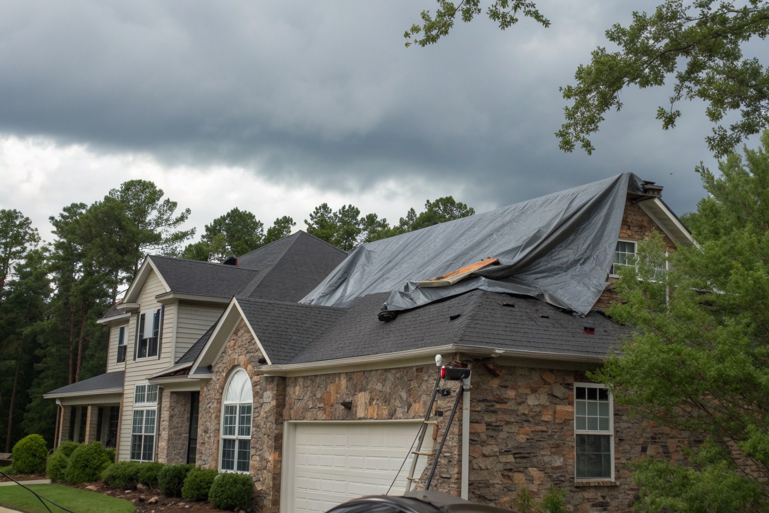 A stone and siding home with a gray tarp over part of its shingle roof after a storm